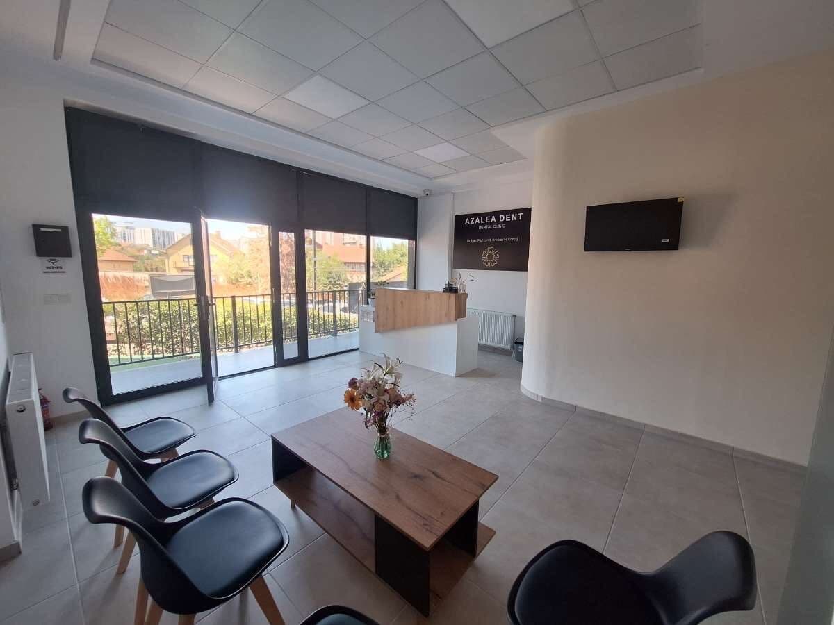 Zona e pritjes e klinikës, me karrige, tavolinë prej druri dhe recepsion përballë dritareve nga dyshemeja në tavan.